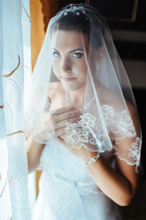 Bride getting ready. beautiful bride in white wedding dress with hairstyle and bright makeup. Happy sexy girl waiting for groom. Romantic lady in bridal dress have final preparation for wedding.の写真素材