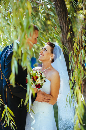 Bride and Groom at wedding Day walking Outdoors on spring nature. Bridal couple, Happy Newlywed woman and man embracing in green park. Loving wedding couple outdoor. Wedding shot of bride and groom in parkの写真素材