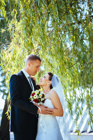 Bride and Groom at wedding Day walking Outdoors on spring nature. Bridal couple, Happy Newlywed woman and man embracing in green park. Loving wedding couple outdoor. Wedding shot of bride and groom in parkの写真素材