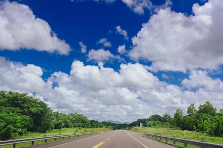 Road crossing the forest with cloudy sky and mountain viewの写真素材