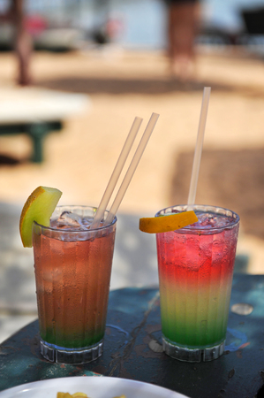Two multi-colored cocktails on the background of the beach. Two glasses with colorful cocktail on a beach near the oceanの写真素材