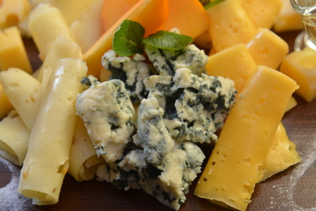 Assorted sliced cheese with mildew, blue, brie, swiss , cheddar, maasdam on the wooden background. fruit and olive oil.の写真素材
