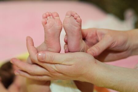 Children's legs in the hands of the mother. Tiny legs of a newborn baby on female hands close-up. Mom and her baby. The concept of a happy family. Concept of health. The treatment.の写真素材
