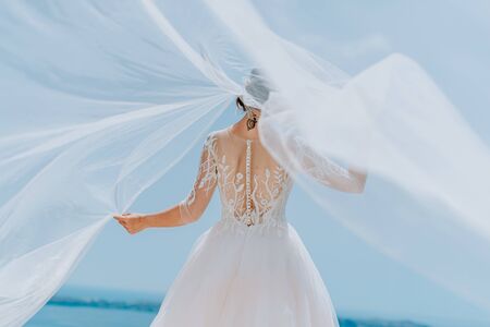 Romantic beautiful bride in white dress posing on terrace with sea and mountains in background.の写真素材
