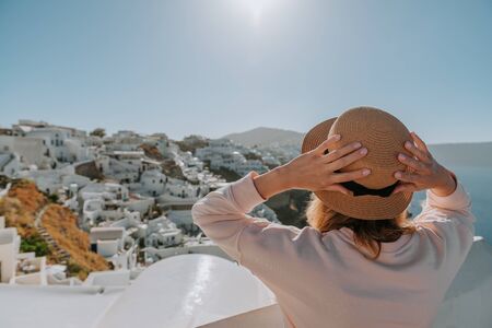 Santorini travel tourist woman on vacation in Oia walking. Girl visiting the famous white village with the mediterranean sea and blue domes. Europe summer destination. Beautiful Girl on the background of the Island of Santoriniの写真素材