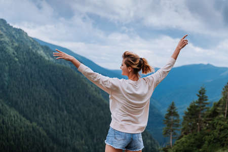 Young woman standing on cliffs edge and looking to a sky with raised handsの写真素材