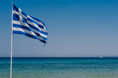 Greek flag on the cliff with blue sea on backgroundの写真素材