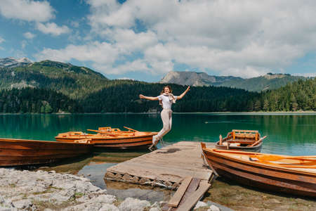 Girl looking to the lake, forest and mountains in Montenegro Durmitor national park. Tourist girl enjoys the magical view of the lake, coniferous forest and magical view sitting on big stone on the shore of a turquoise lake in the mountains. Hiking in the Natural Park. Black lake.の写真素材