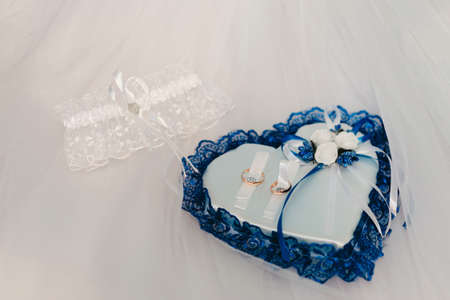 Wedding accessories for the bride, luxury ring pillow and garter, classic leather shoes, elegance veil with lace. Selective focus. Bride's shoes and Bride's garter with bride and groom wedding rings on the pillow, close-up.の写真素材