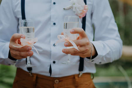 Handsome groom holding two glasses of champagne. Handsome happy man in elegant suit holding holding two glasses of champagne and celebrating his wedding dayの写真素材