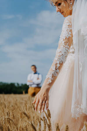 fashionable and happy wedding couple at wheat field at sunny day. Bride and groom kissing in a wheat field. Young beautiful wedding couple hugging in a field with grass eared.の写真素材