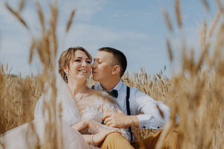 fashionable and happy wedding couple at wheat field at sunny day. Bride and groom kissing in a wheat field. Young beautiful wedding couple hugging in a field with grass eared.の写真素材