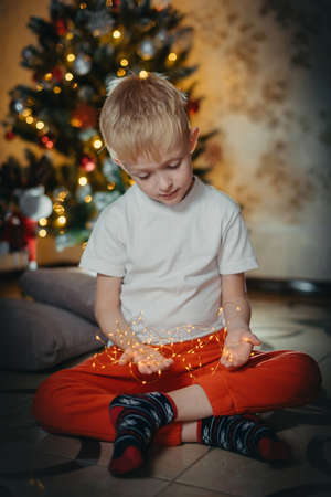 adorable little baby boy sitting in front of a christmas tree. Christmas Child Open Present Gift, Happy Baby Boy looking to Magic Light in Box, Kid sitting front of Xmas Treeの写真素材