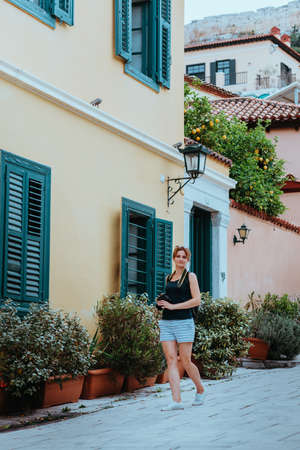 Beautiful girl walking along the street of an old European town with a film camera in her hand. Portrait of a tourist girl walking on the street background.の写真素材