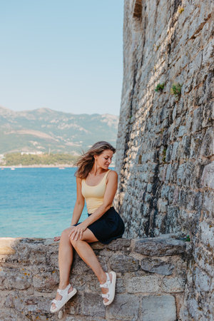Beautiful girl sitting on a stone wall, in background is the blue sea, Budva, Montenegro.