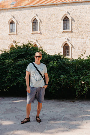 A handsome young man standing and smiling happily in the background of urban buildings. Forty years old caucasian tourist man outdoor near old city buildings - summer holiday.の写真素材