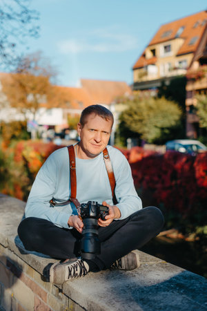 Man Sitting in Old European City And Holding Photo Camera. Contemporary Stylish Blogger And Photographer. Handsome man taking a selfie on a trip in Europe.の写真素材