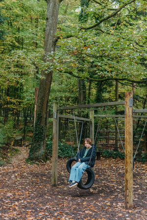A teenage girl sitting on a swing on the park. Pensive sad child. Thoughtful Sad Teenager Girl Sitting On Playground Roundabout. teenage girl sad on the swing in the park.の写真素材