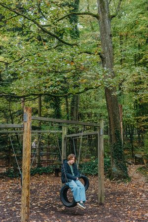A teenage girl sitting on a swing on the park. Pensive sad child. Thoughtful Sad Teenager Girl Sitting On Playground Roundabout. teenage girl sad on the swing in the park.の写真素材