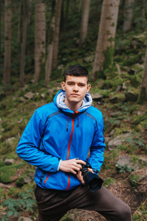 Young Caucasian Male Photographer Taking Picture in the autumn park. Photographer man holding camera in the woods. Photographer man taking a photo outdoor traveling. A photographer with his camera in hand in the mountain forest. The landscape with forests, mountains. Travel or adventure concept.の写真素材