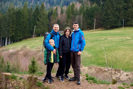 Young family enjoying their holidays in a national park. Caucasian family walking down a mountain trail and having fun. Family hiking on vacation, standing with arms around on top of the mountain, looking at beautiful summer mountains landscape. People enjoying beautiful view.の写真素材