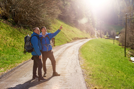 Two hikers are in the mountains in the spring nature outdoor. Hiking with backpacks. Two friends travel together in picturesque places. The man shows the way. Two men on a hiking trip in the mountains. Tourists on a trekking route in Germany.の写真素材