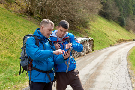 Two hikers are in the mountains in the spring nature outdoor. Hiking with backpacks. Two friends travel together in picturesque places. The man shows the way. Two men on a hiking trip in the mountains. Tourists on a trekking route in Germany.の写真素材