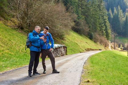 Two hikers are in the mountains in the spring nature outdoor. Hiking with backpacks. Two friends travel together in picturesque places. The man shows the way. Two men on a hiking trip in the mountains. Tourists on a trekking route in Germany.の写真素材