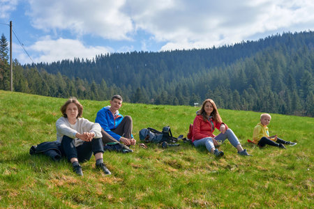 Happy family sitting on grass outdoors in park. happy young family spending time outdoor on a summer dayの写真素材