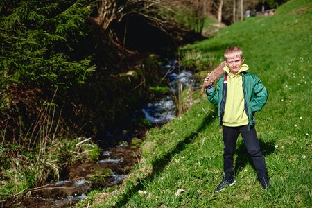 A little boy walks along a mountain river. Through the clear water, he examines the pebbles at the bottom of the riverの写真素材