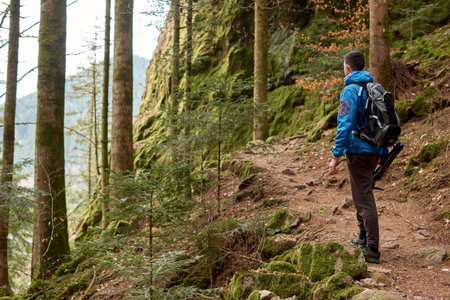 Traveler Man with backpack mountaineering Travel Lifestyle concept mountains on background Summer trip vacations outdoor. Concept of travel and healthy, active lifestyle. Young guy with dreadlocks went hiking in mountains. Man with yellow backpack stands on top of hill and enjoys views of nature. A guy tourist with a backpack stands on a mountain trail and looks into the distance. The concept of travel and adventure.の写真素材
