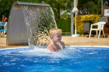 Young boy kid child eight years old splashing in swimming pool having fun leisure activity. Boy happy swimming in a pool. Activities on the pool, children swimming and playing in water, happiness and summertimeの写真素材