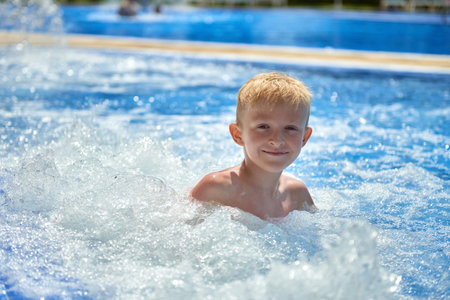 Young boy kid child eight years old splashing in swimming pool having fun leisure activity. Boy happy swimming in a pool. Activities on the pool, children swimming and playing in water, happiness and summertimeの写真素材