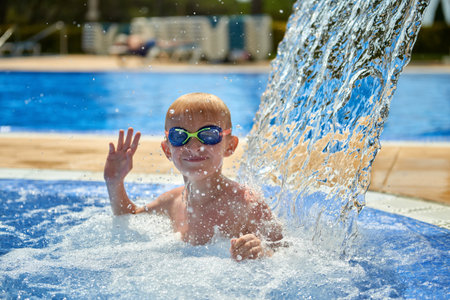 Young boy kid child eight years old splashing in swimming pool having fun leisure activity. Boy happy swimming in a pool. Activities on the pool, children swimming and playing in water, happiness and summertimeの写真素材