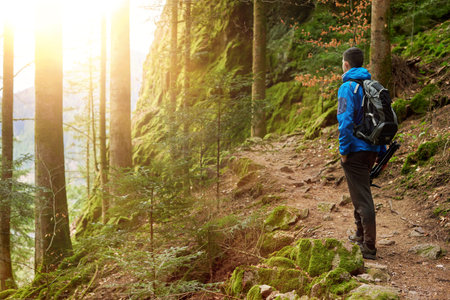 Traveler Man with backpack mountaineering Travel Lifestyle concept mountains on background Summer trip vacations outdoor. Concept of travel and healthy, active lifestyle. Young guy with dreadlocks went hiking in mountains. Man with yellow backpack stands on top of hill and enjoys views of nature. A guy tourist with a backpack stands on a mountain trail and looks into the distance. The concept of travel and adventure.の写真素材