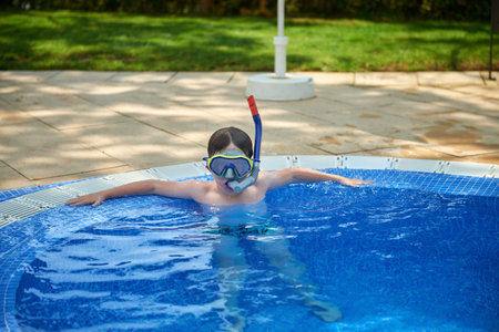 Young boy kid child eight years old splashing in swimming pool having fun leisure activity. Boy happy swimming in a pool. Activities on the pool, children swimming and playing in water, happiness and summertimeの写真素材