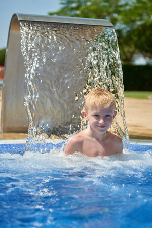 Young boy kid child eight years old splashing in swimming pool having fun leisure activity. Boy happy swimming in a pool. Activities on the pool, children swimming and playing in water, happiness and summertimeの写真素材