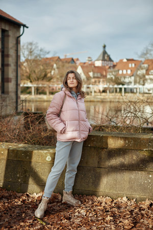 Young beautiful pretty tourist girl in warm hat and coat with backpack walking at cold autumn in Europe city enjoying her travel in Bietigheim-Bissingen, Deutschland. Outdoor portrait of young tourist woman enjoying sightseeingの写真素材