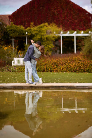 Young couple kissing and rejoices at the lake. lovely young couple kissing outdoors in autumn. Loving couple walking in nature. Autumn mood. Happy man and woman hugging and kissing in autumn. Love. Fashionable couple outdoors. Fashion, people and lifestyle. Stylish couple in autumn outfit.の写真素材