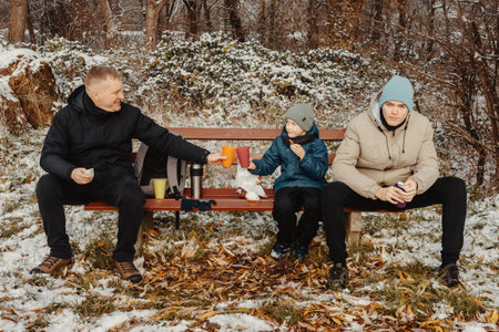 Snowy Park Serenity: Dad and Sons Share Treats and Smiles in a Winter Wonderland. Winters Togetherness: A Delightful Bench Picnic with Dad and the Boys. A Heartwarming Winter Picnic with Father and Sons in a Snow-Kissed Parkの写真素材