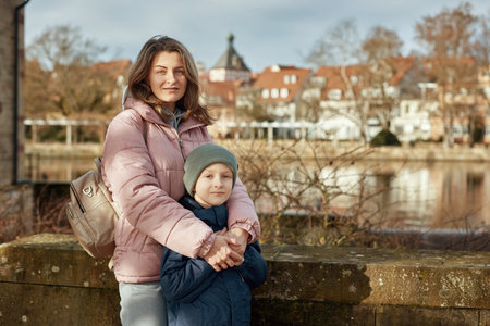 Riverside Family Harmony: Mother, 30 Years Old, and Son - Beautiful 8-Year-Old Boy, Standing by Neckar River and Historic Half-Timbered Town, Bietigheim-Bissingen, Germany, Autumnの写真素材