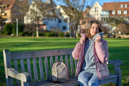 Winter Joy in Bitigheim-Bissingen: Beautiful Girl in Pink Jacket Sitting Amidst Half-Timbered Charm. beautiful girl in a pink winter jacket sitting on a bench in a park, set against the backdrop of the historic town of Bitigheim-Bissingen, Baden-WÃ¼rttemberg, Germany.の写真素材