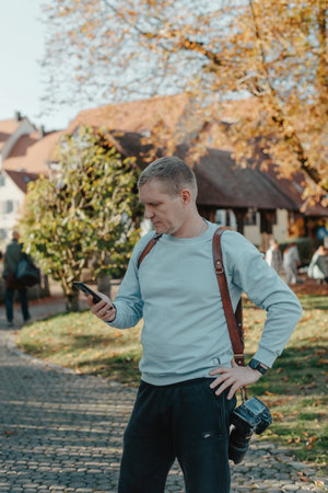Professional Photographer Taking Picture Of Beautiful Autumn Park. Man Professional Photographer standing With Camera And With Smartphone In Autumn Park. Retouched, Vibrant Colorsの写真素材