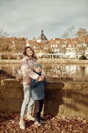 Riverside Family Harmony: Mother, 30 Years Old, and Son - Beautiful 8-Year-Old Boy, Standing by Neckar River and Historic Half-Timbered Town, Bietigheim-Bissingen, Germany, Autumnの写真素材
