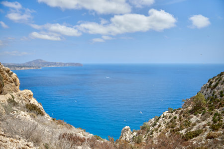 Breathtaking Panoramic View of Calpes Turquoise Bay from Majestic Cliffside Overlooking Iconic Penon de Ifach Rock Formation. Stunning Costa Blanca Seascape: Calpes Golden Beaches and Azure Waters Framed by Dramatic Cliffs and Cloudscapeの写真素材