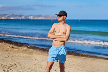Cool Nineteen-Year-Old Vacationer Enjoying Costa Blanca Paradise at Calpes Breathtaking Beach Beneath Majestic Rock Formation. Fashion-Forward Teen Exploring Calpes Stunning Shoreline with Sunglasses and Capの写真素材
