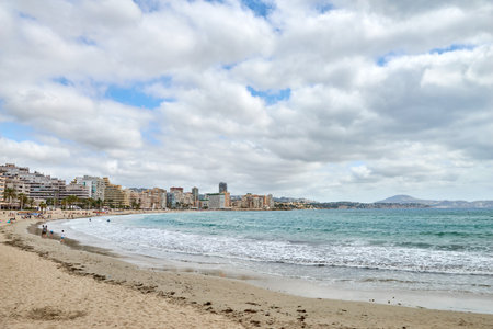 Stunning panoramic view of Calpe Spain with turquoise sea dramatic sky and beachfront hotels on a sunny summer day European vacation destination. Calpe Spain coastal landscape with rocky shore turquoise waters sandy beach and hotels under dramatic summer sky travel and tourismの写真素材