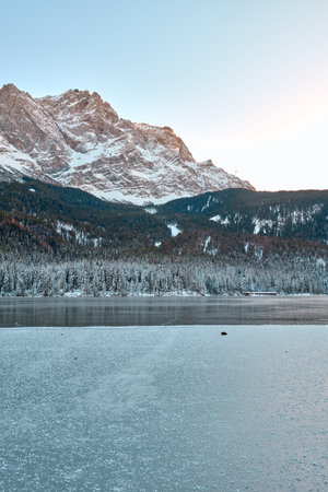 Breathtaking Alpine Winter Wonderland: Majestic Mountain Reflects in Frozen Lake Amidst Snowy Landscape Picturesque Ski Resort Nestled in Forest Offers Stunning Panoramic Views of Pristine Icy Scenery.の写真素材