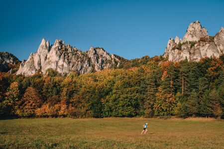 Man running on the autumn meadow near by majestic rocky hillsの写真素材