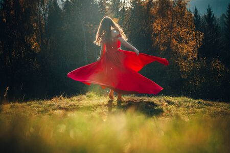 Mysterious sorceress in a beautiful red dress. Her hair and dress are fluttering in the wind. Background bright, autumn,の写真素材